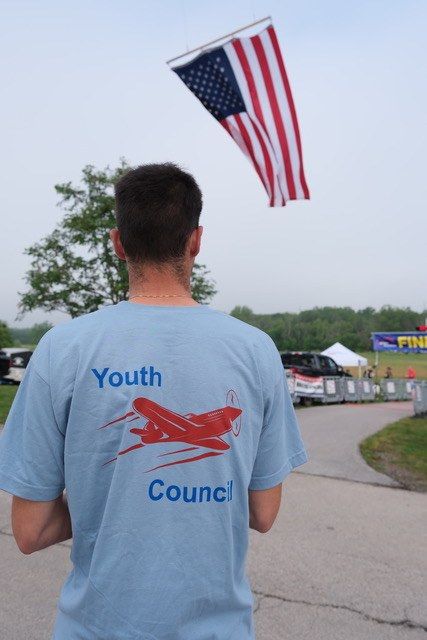 Youth Council member in a council shirt beneath a large American flag