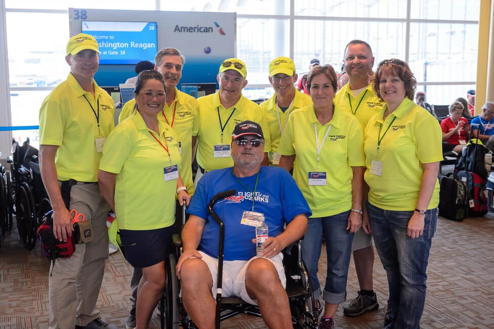 Honor Flight volunteers standing around a sitting veteran