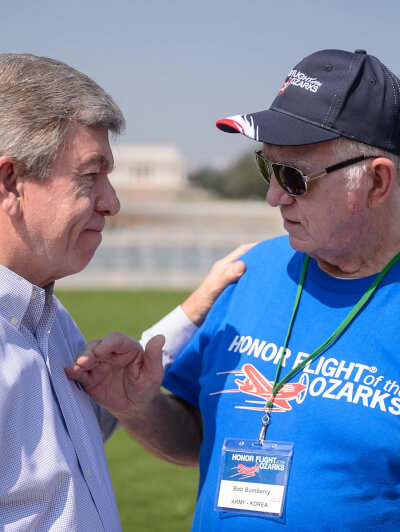 Honor Flight Veteran with Guardian next to American Flag